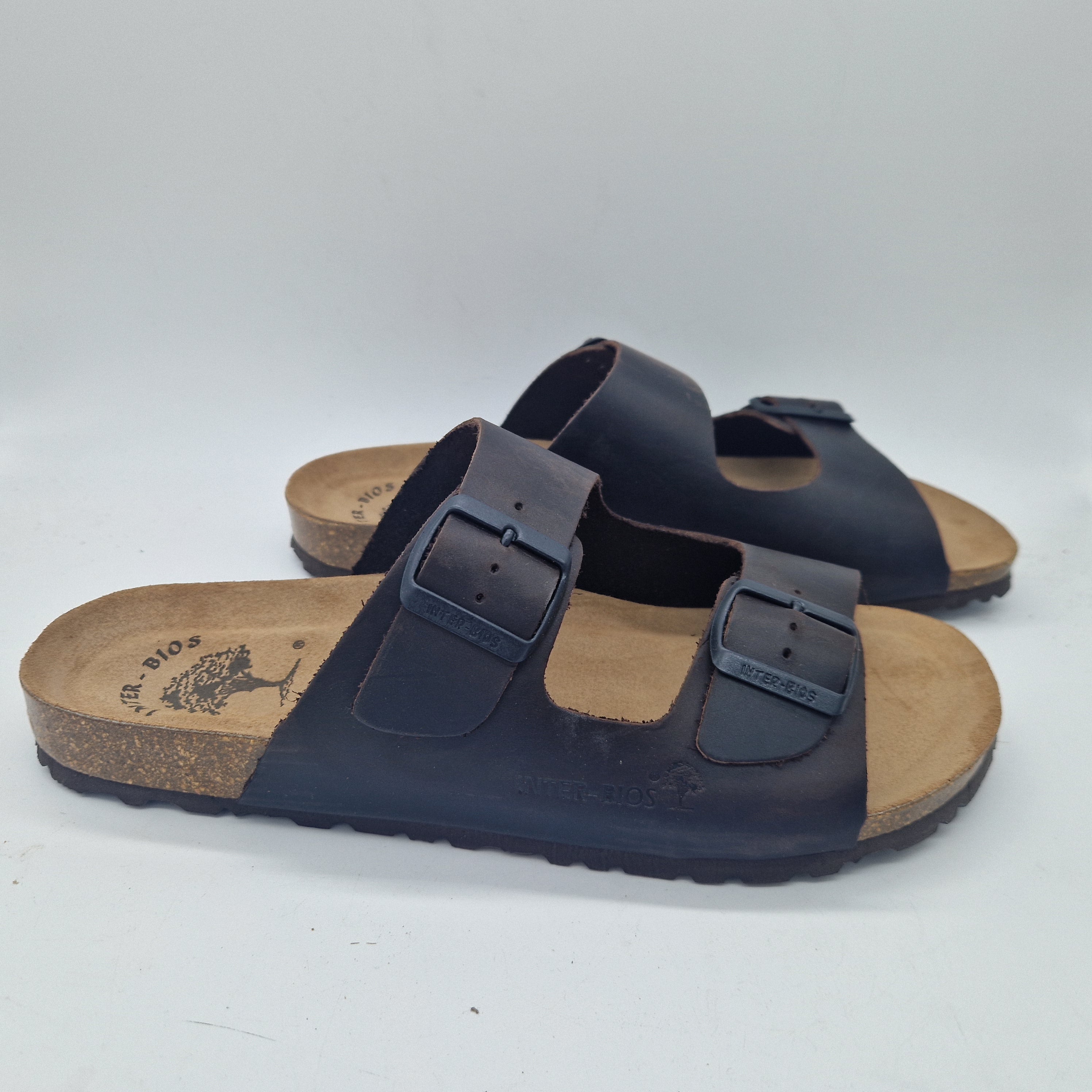 Sandalias Interbios de dos hebillas en marrón, con piso fino, vistas desde un ángulo que muestra las correas y el diseño elegante.